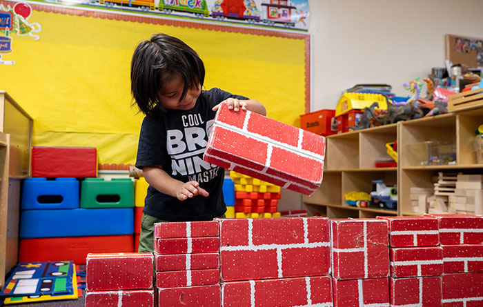 A young boy stacking large red blocks in a kindergarten classroom.