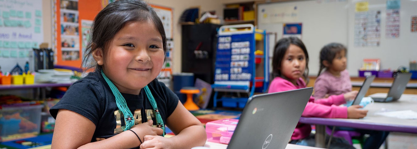 Three female students working on laptops while smiling at the camera. 