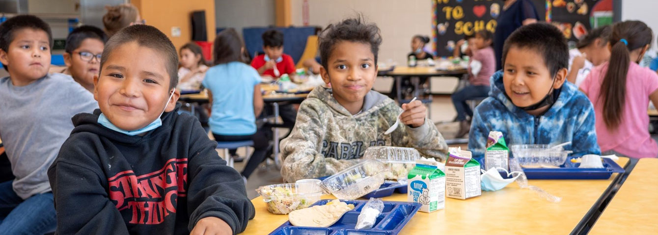 Jeehdeez'a Elementary School cafeteria with students eating lunch while smiling at the camera.