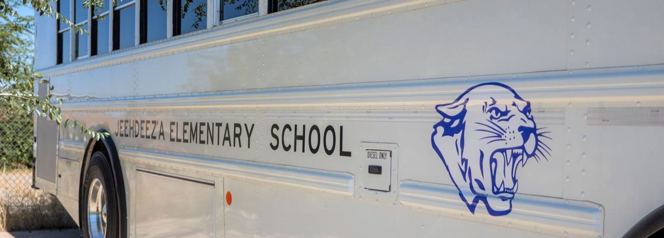 Side view of Jeehdeez'a Elementary school bus displaying the logo.